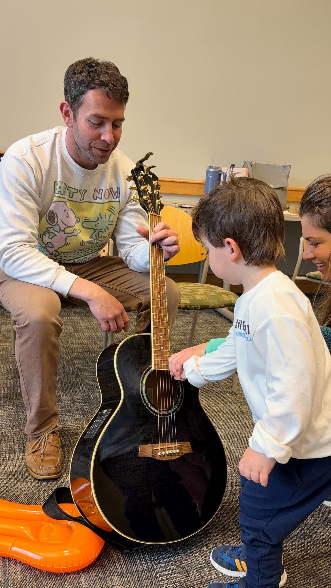 A dad showing his son the strings of an acoustic guitar during class